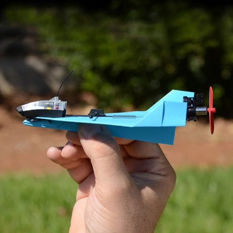 Tech but outdoors! Image of an airplane with a hand holding it outside in green grass