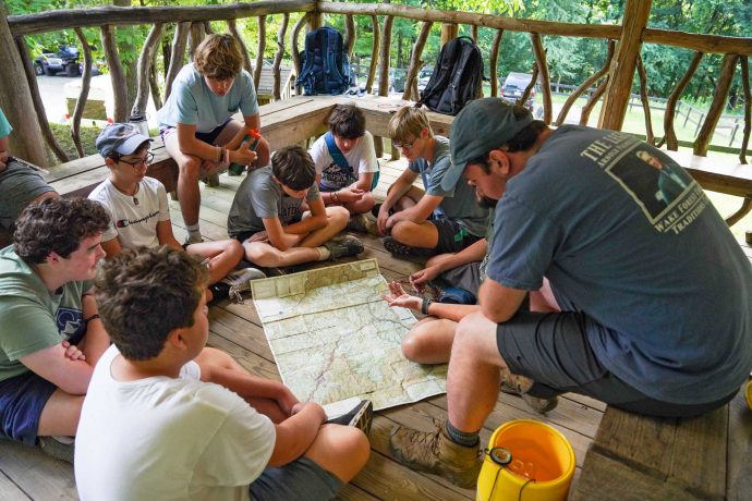 Campers sitting leaning over a map with counselor guide.