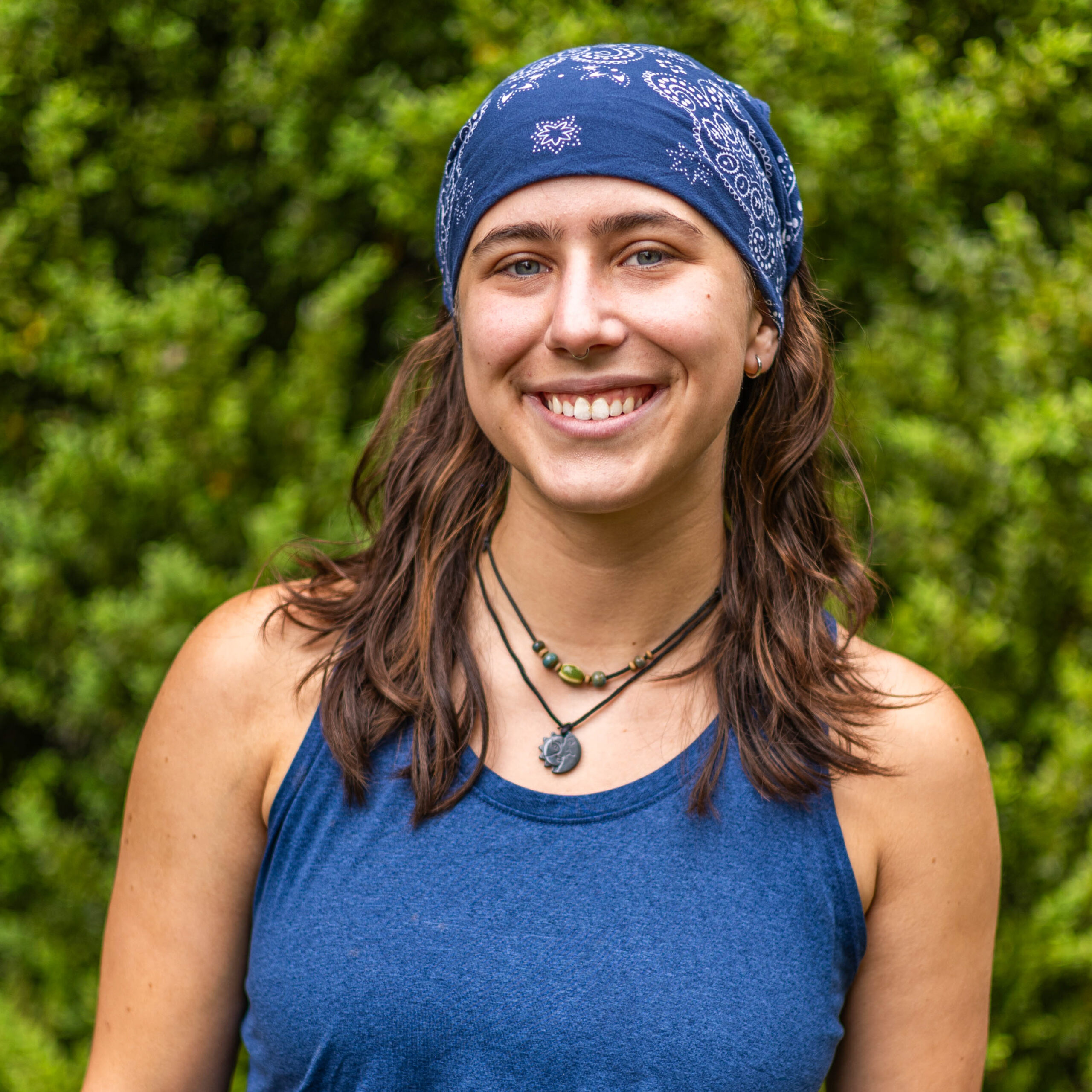 Smiling woman wearing a blue bandana outdoors with green foliage in the background.