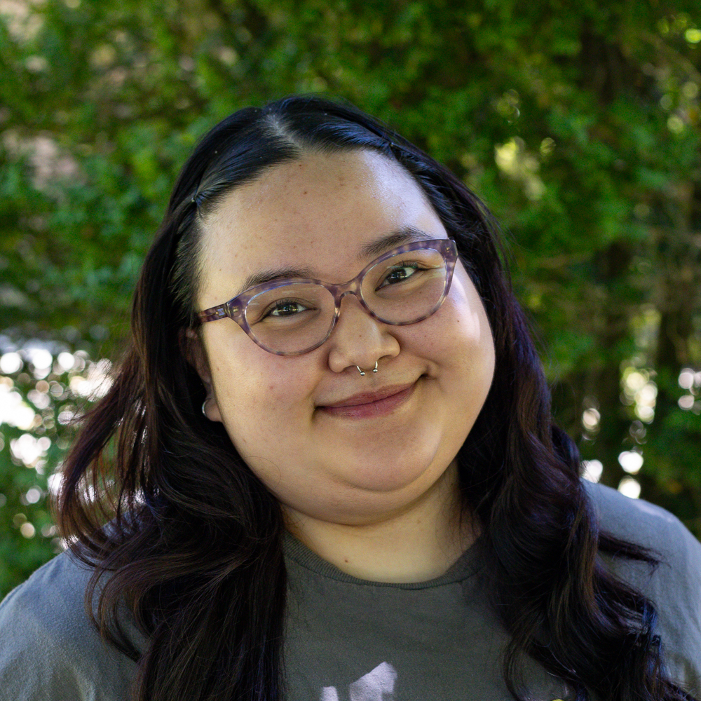 Smiling woman with round glasses outdoors in a green park setting.