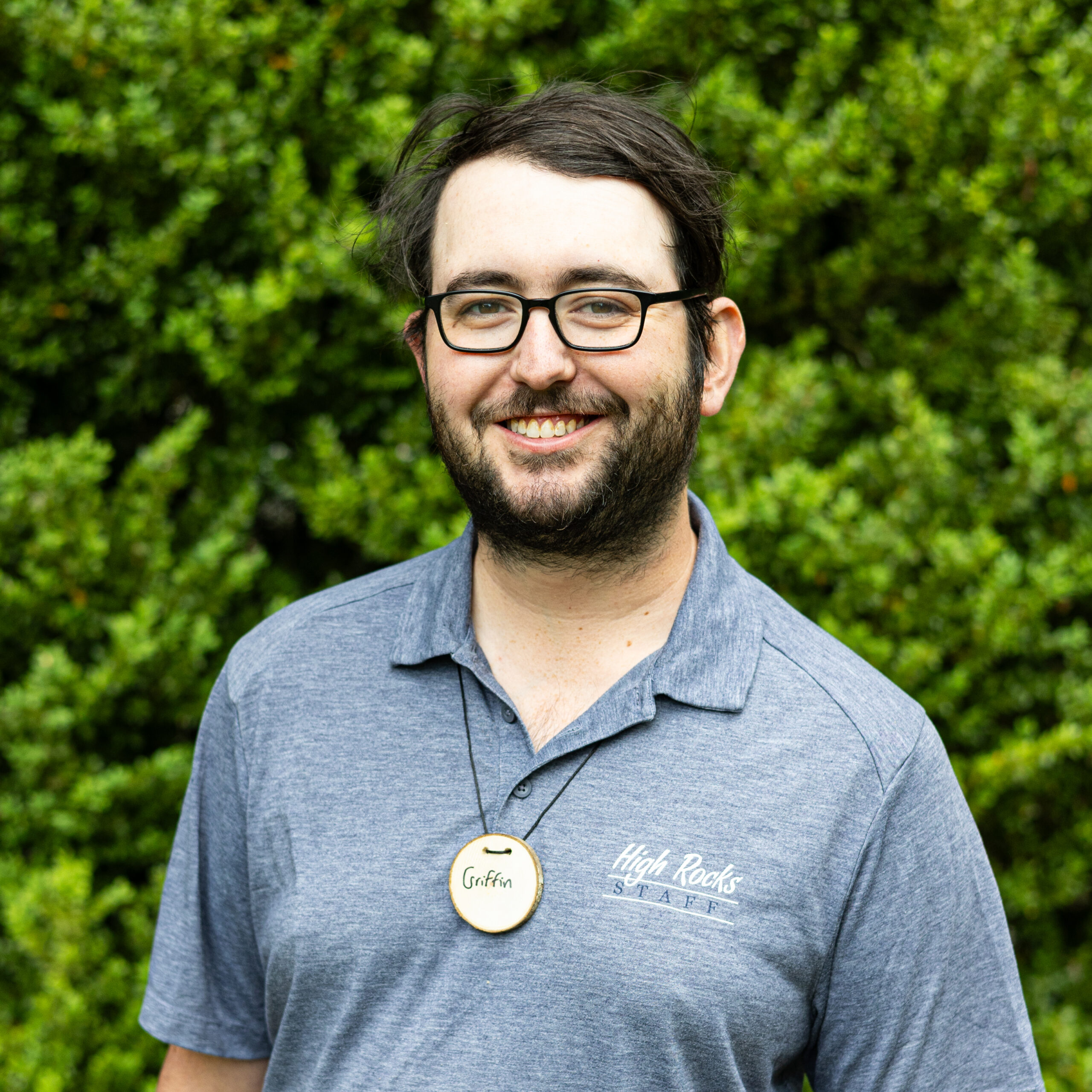 Smiling man with glasses and beard outdoors, wearing a blue-gray shirt and a circular badge that reads Griffin.