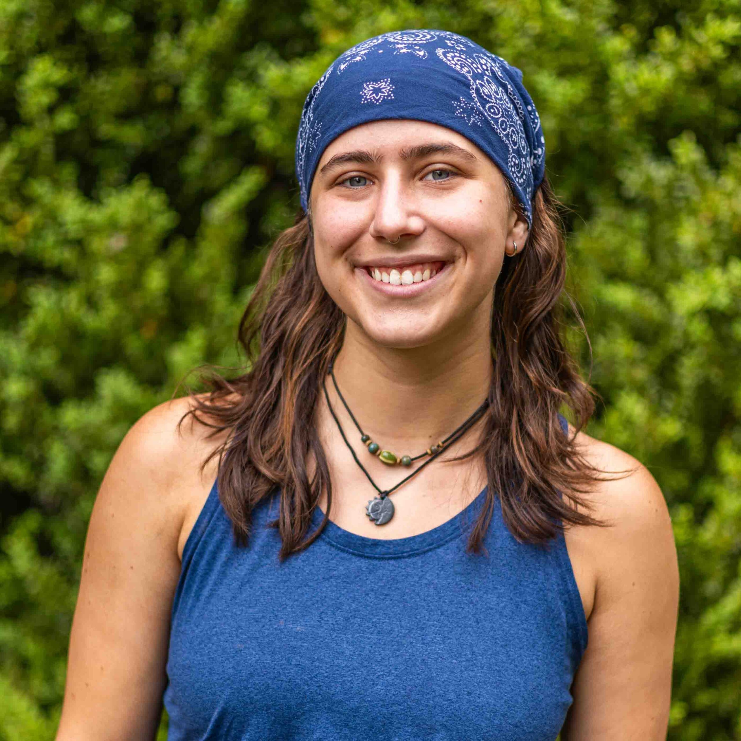 Smiling woman wearing a blue bandana outdoors with green foliage in the background.