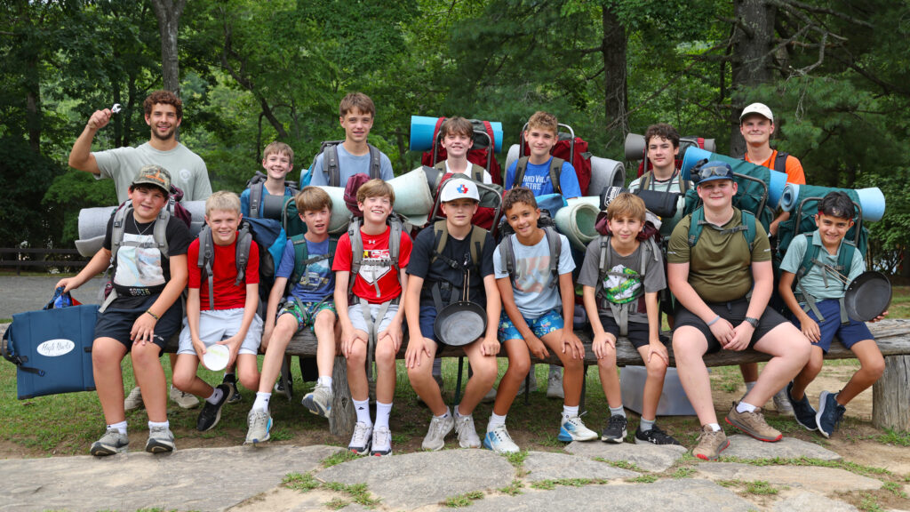 Group of boys with hiking backpacks posing for a photo outdoors in a forested area.